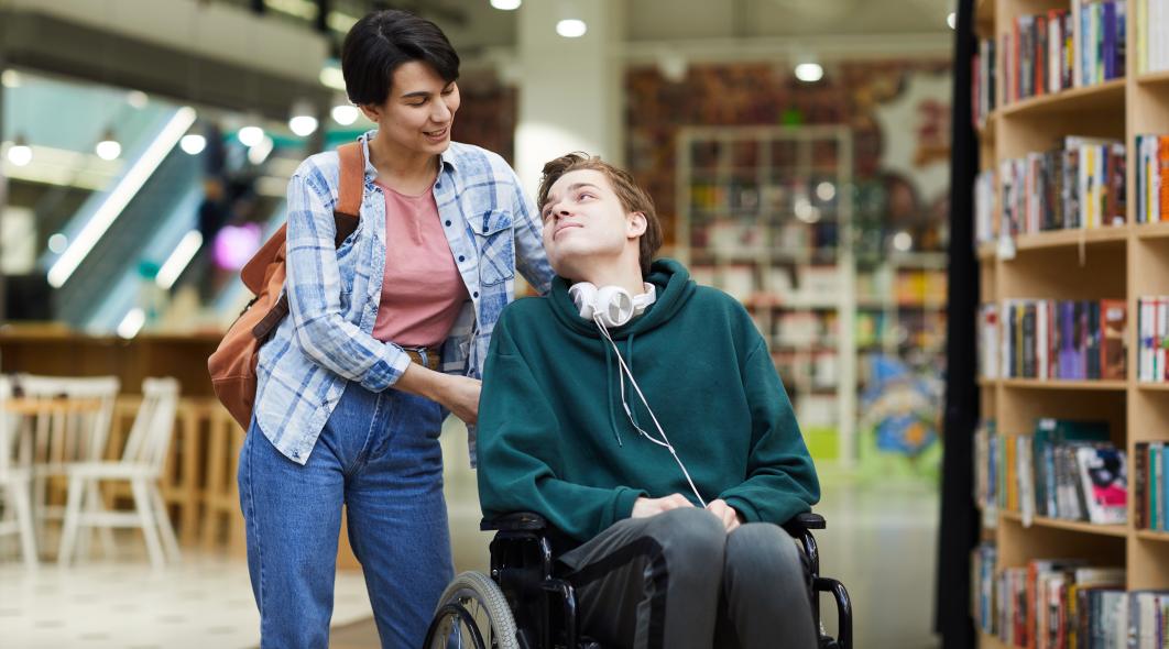 young man in wheelchair with a caregiver looking down and smiling